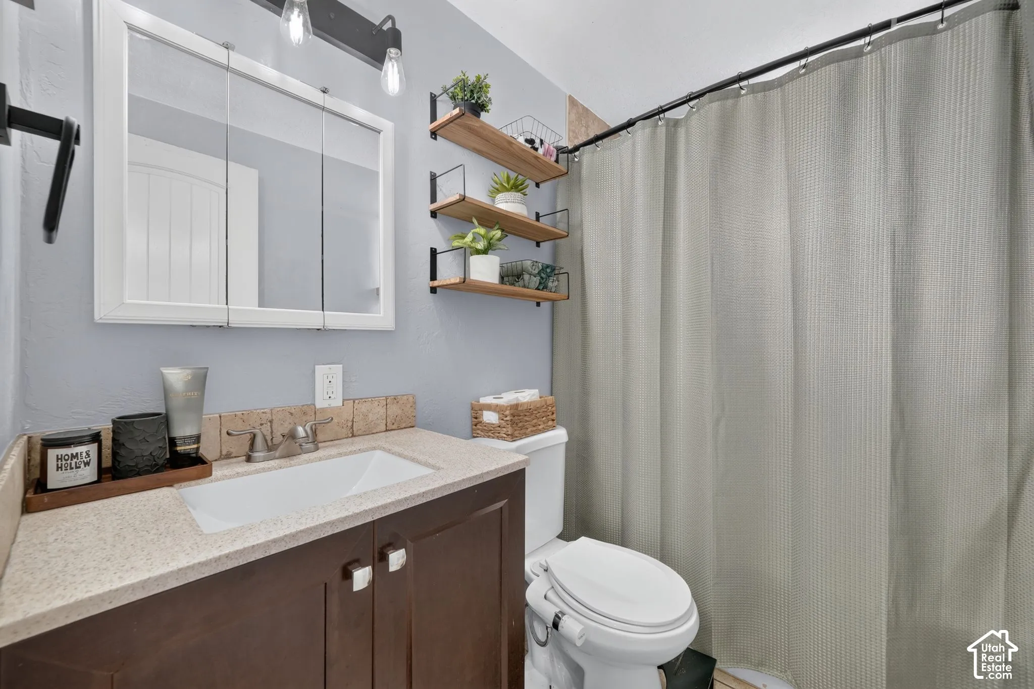 Vanity cabinet with a solid surface countertop, integrated rectangular sink, wall-mounted three-tier shelving system, tri-fold medicine cabinet, and industrial-style vanity lighting