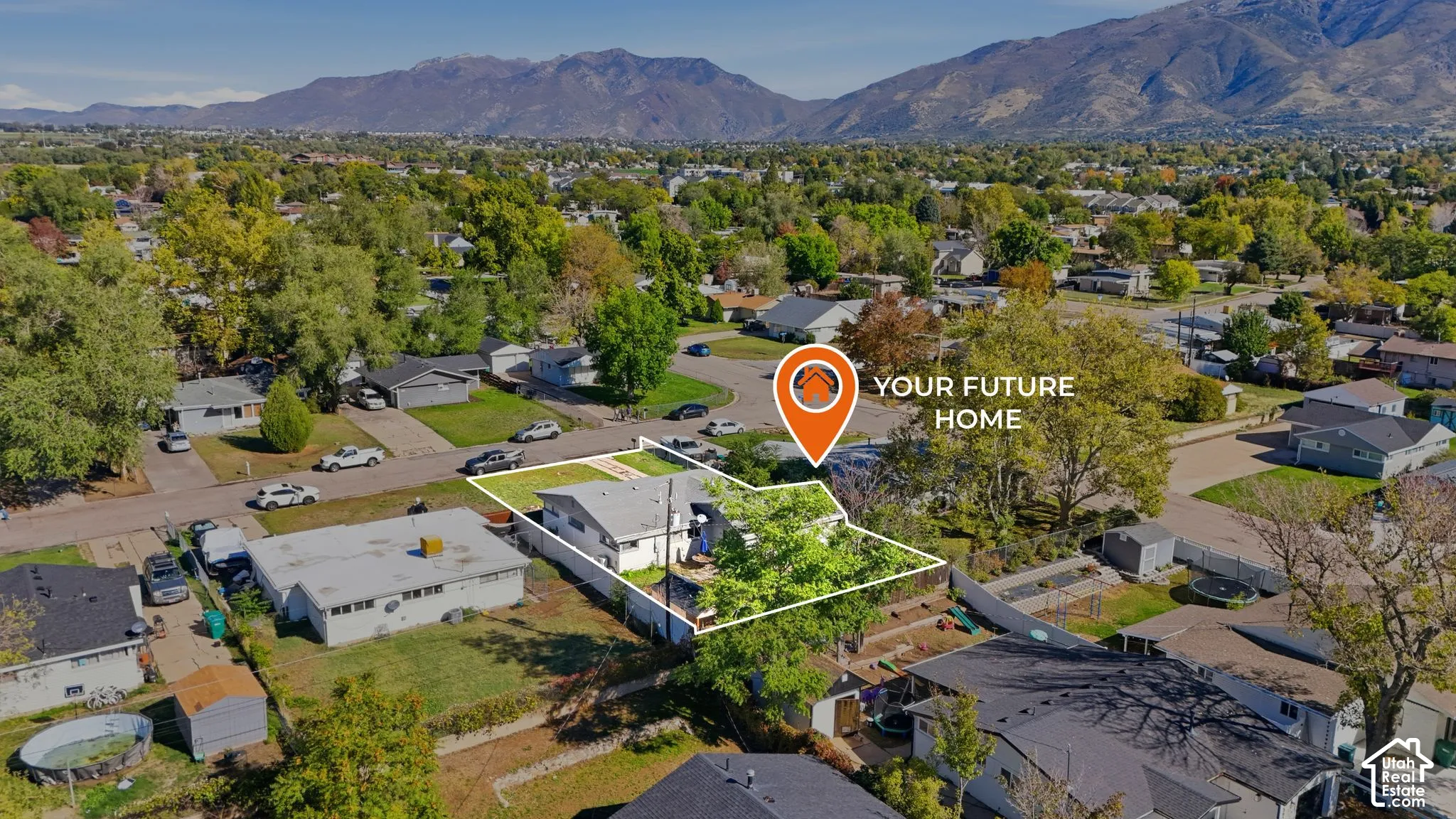 Aerial perspective of a single-story residence featuring a low-slope roof, mature trees, fenced backyard, and backdrop of mountain scenery