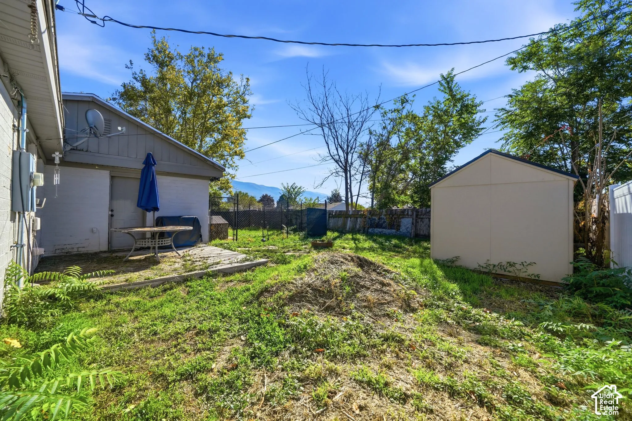 Rear exterior space featuring a concrete patio, detached storage shed, perimeter fencing, and mature trees against a mountain backdrop