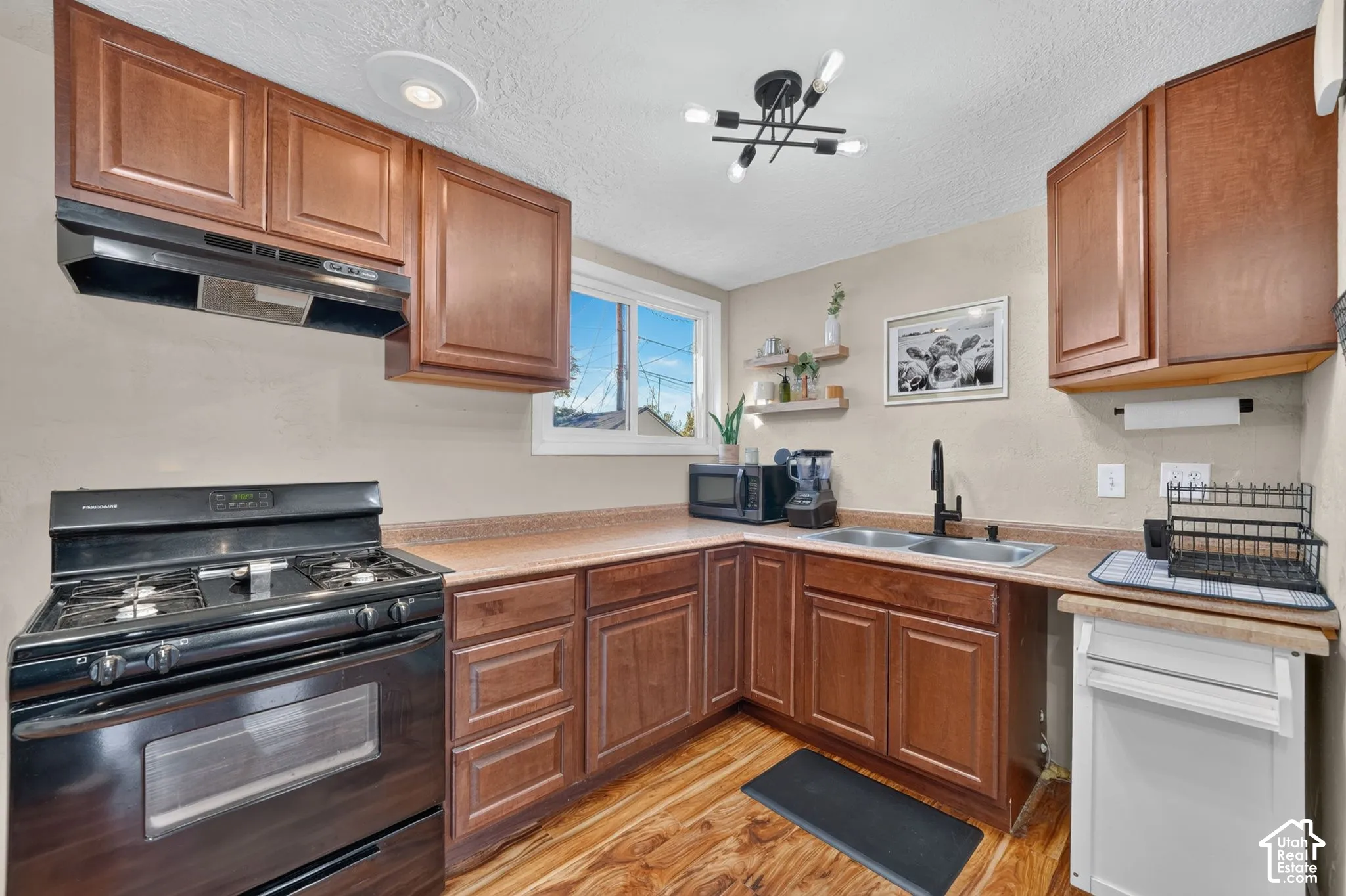 Kitchen featuring stained wood cabinetry, solid surface countertops, a matte black dual-handle faucet, a gas range with matching vent hood, and wood-finish flooring
