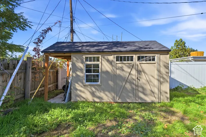 Exterior storage structure featuring a gabled roof, double-door entry with transom windows, a single-hung window with muntins, and a covered side porch