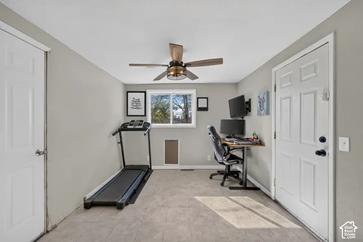 Neutral-toned room featuring tile flooring, a multi-blade ceiling fan with integrated light fixture, a sliding window, and a paneled exterior door