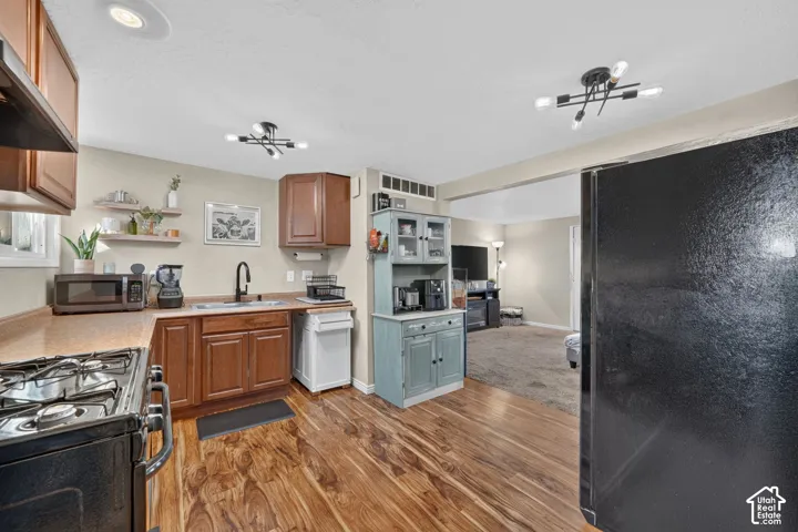 Kitchen featuring wood-finish flooring, warm-toned cabinetry, a matte black kitchen faucet, and modern multi-light ceiling fixtures