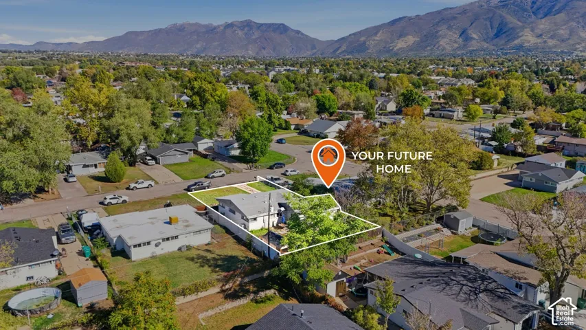 Aerial perspective of a single-story residence featuring a low-slope roof, mature trees, fenced backyard, and backdrop of mountain scenery