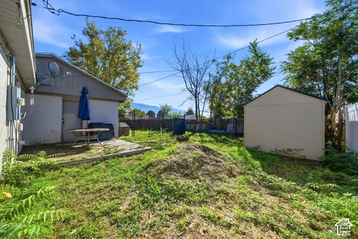 Rear exterior space featuring a concrete patio, detached storage shed, perimeter fencing, and mature trees against a mountain backdrop