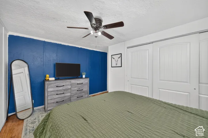 Wood-finish flooring, ceiling fan with integrated lighting, textured accent wall, and sliding closet doors with recessed panel detailing