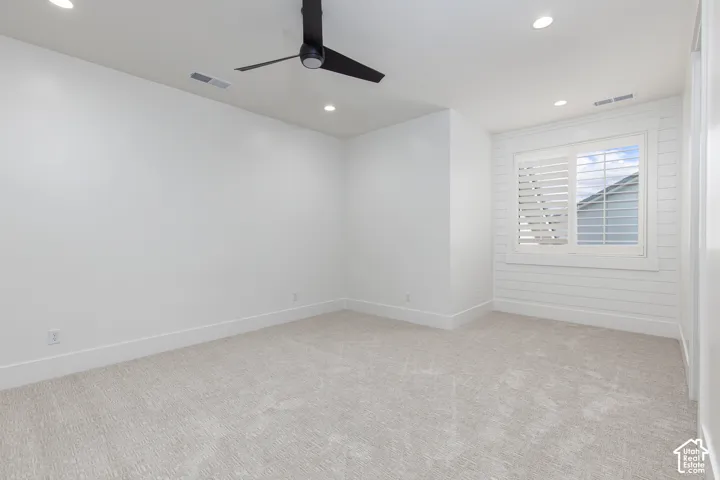 Interior space featuring neutral carpeting, recessed ceiling lighting, a matte black ceiling fan, white horizontal wall paneling, and plantation shutters