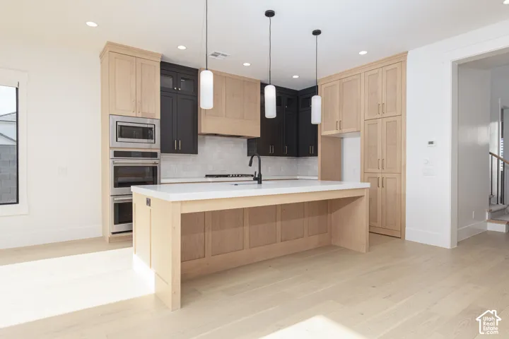 Kitchen featuring two-tone cabinetry, central island with light-toned finish and stone-surface countertop, built-in stainless steel double wall oven, and three glass pendant lights