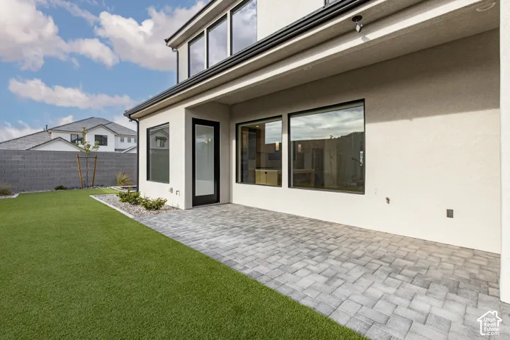 Stucco exterior featuring a covered paver patio, synthetic lawn, and large windows with black frames
