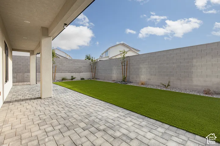 Covered patio featuring paver flooring, synthetic turf lawn, and a concrete block perimeter wall