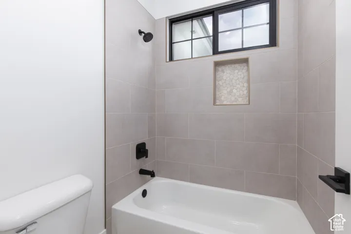 Shower and tub combination featuring large-format wall tile, matte black fixtures, an integrated pebble-tile inlay niche, and a multi-pane window