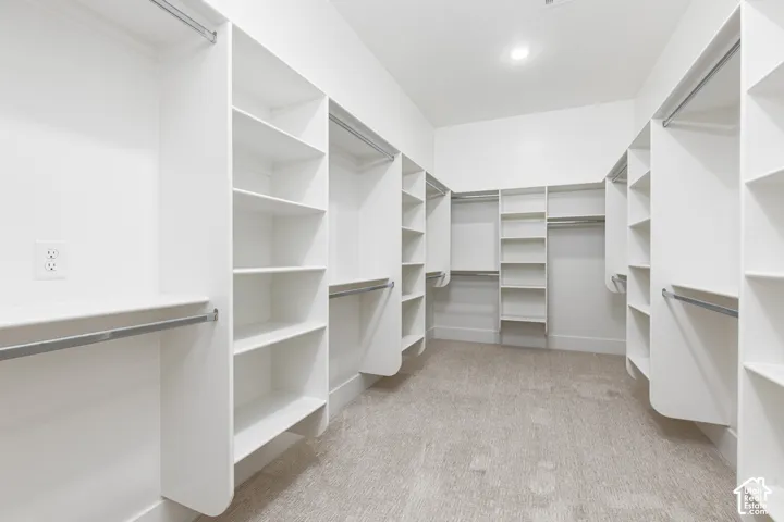 Walk-in closet featuring extensive built-in white shelving, multiple hanging rods, recessed ceiling lighting, and carpeted flooring