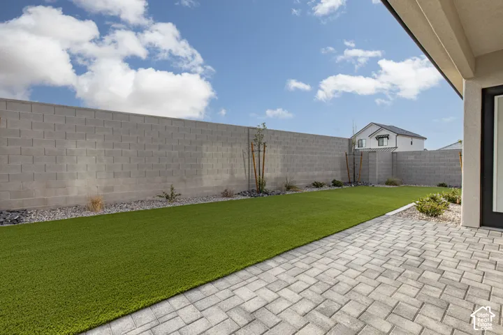 Rear exterior featuring a paver stone patio, artificial turf lawn, concrete masonry unit perimeter wall, and stone ground cover
