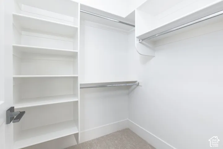 Walk-in closet featuring white built-in shelving, dual-level metal hanging rods, and neutral carpeting