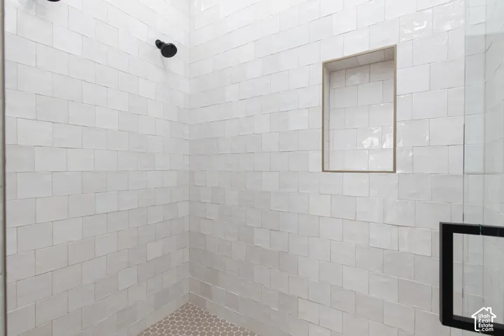 Walk-in shower featuring glossy white square wall tile, a recessed storage niche, round mosaic floor tile, and matte black fixtures