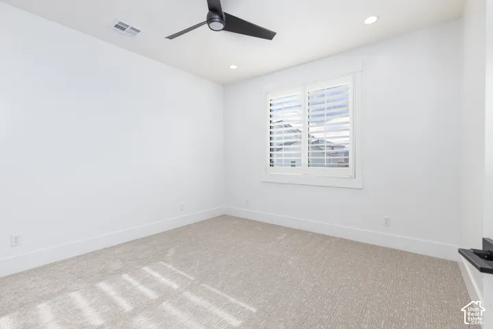 Room interior featuring neutral carpeting, a matte black three-blade ceiling fan, recessed lighting, and a window accented by white plantation shutters