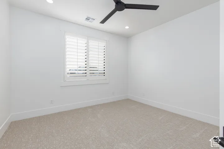 Neutral-toned wall-to-wall carpeting, matte black ceiling fan, white plantation shutters, and recessed lighting