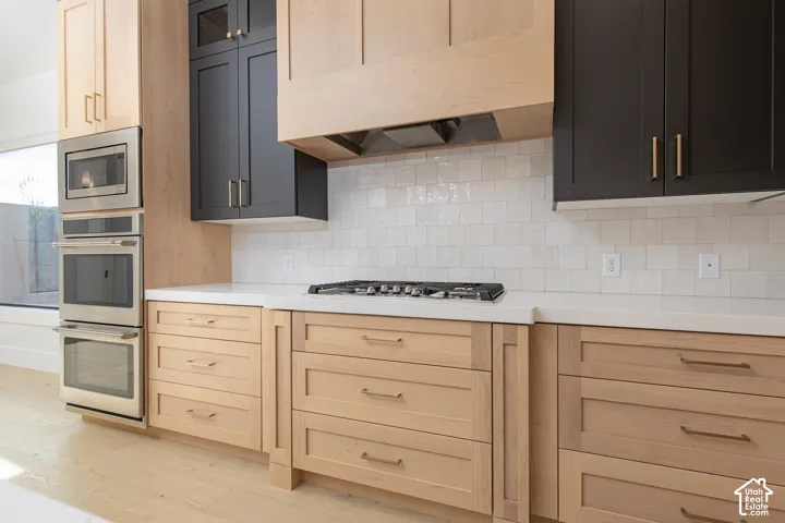 Two-tone cabinetry featuring light wood finish and matte black shaker-style uppers, integrated wooden range hood, white quartz countertops, handmade-style ceramic tile backsplash, and built-in stainless steel double wall oven