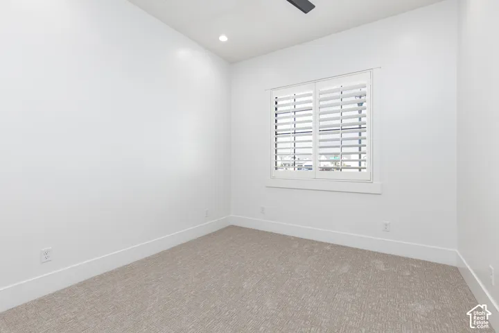 Neutral-toned wall-to-wall carpeting, recessed ceiling lighting, and window featuring white plantation shutters with trim casing