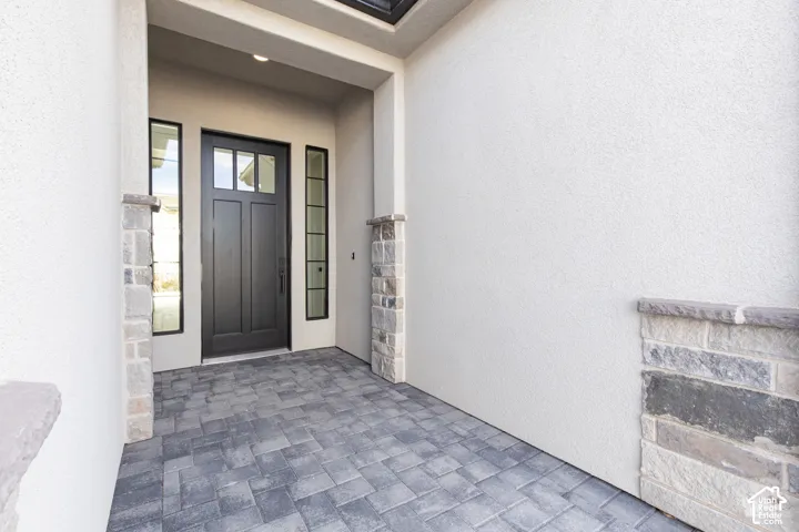 Covered entryway featuring a paver floor, textured stucco walls, stacked stone accents, and a dark-finish door with sidelights