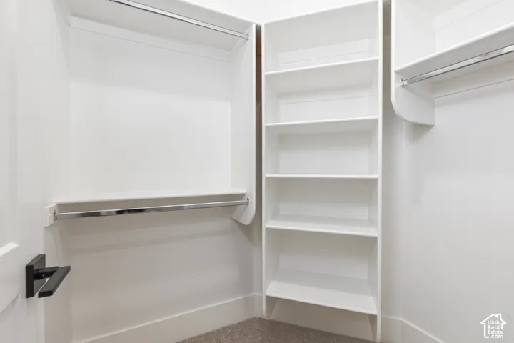 Walk-in closet featuring white built-in shelving, dual hanging rods, and a matte black door handle