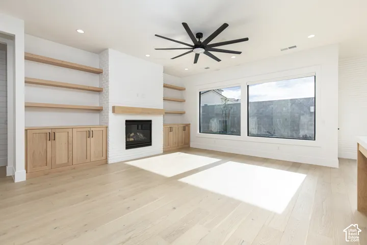 Living area featuring wood-finish flooring, a white-painted brick fireplace with a wood mantel, built-in cabinetry, floating shelves, and a multi-blade ceiling fan