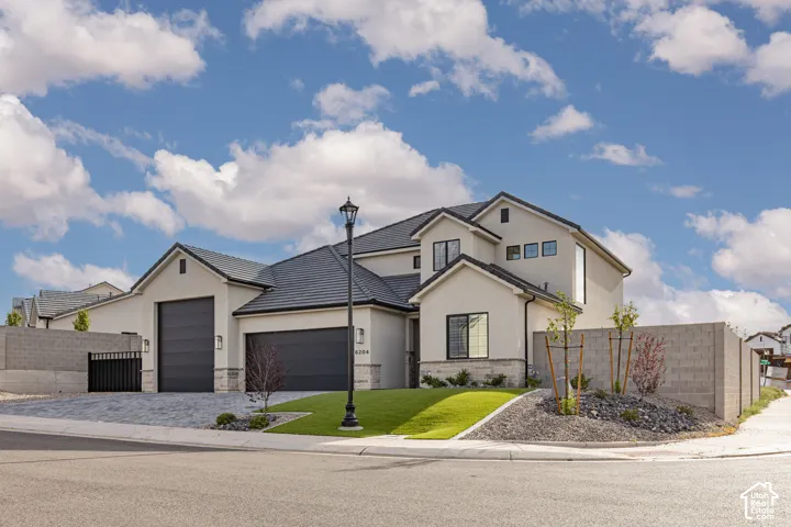 Multi-level exterior featuring stucco siding, stone veneer accents, a dark-toned tile roof, and an attached multi-car garage with a paved driveway