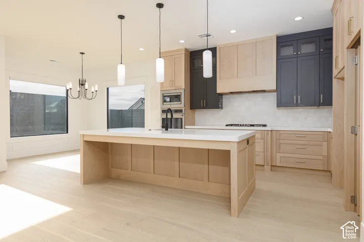 Kitchen featuring dual-toned flat-panel cabinetry, a central island with a solid surface countertop, wood-finish flooring, built-in stainless steel double ovens, and recessed lighting