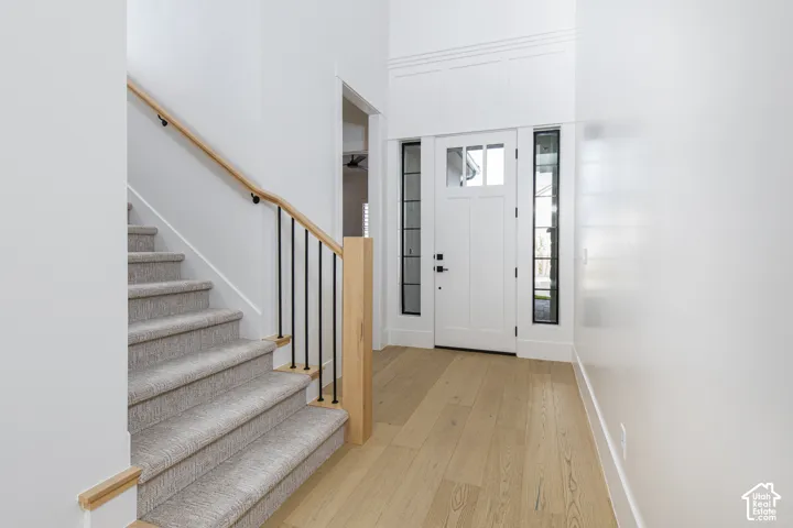 Entryway featuring high ceilings, wood-finish flooring, a white front door with side glass panels, and a staircase with light wood handrails and black metal spindles