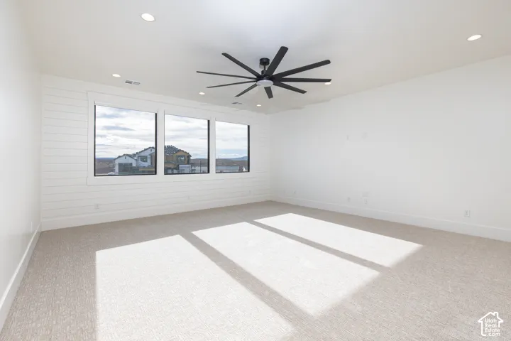 Expansive interior space featuring horizontal shiplap wall detailing, neutral carpeting, large windows, recessed lighting, and a multi-blade ceiling fan