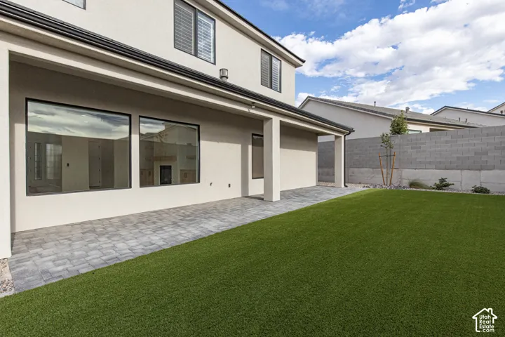 Covered patio featuring paver flooring, synthetic turf lawn, and masonry perimeter wall