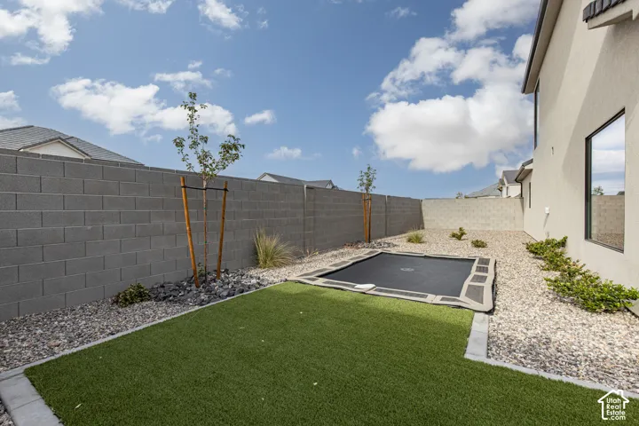 Low-maintenance backyard featuring synthetic turf, an in-ground trampoline, decorative rock landscaping, and a concrete block perimeter wall