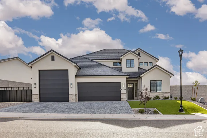 Stucco exterior featuring multi-level rooflines, tile roofing, stone veneer accents, multi-car garage, and paved driveway