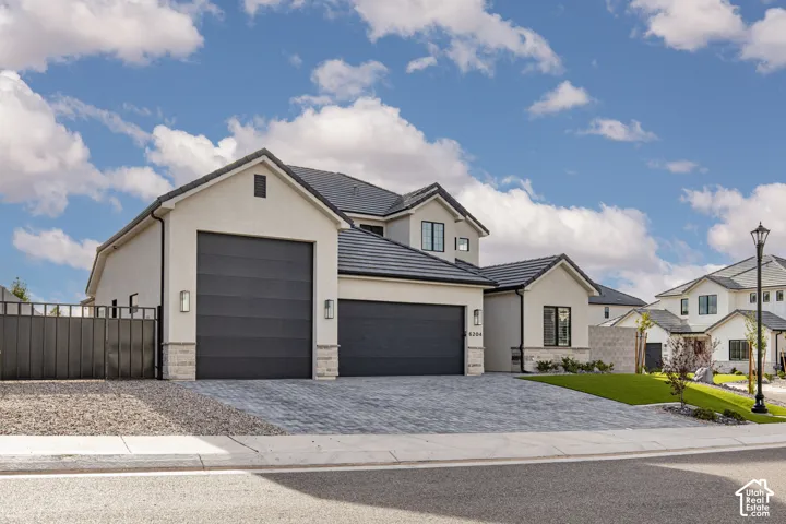 Stucco exterior featuring dual garages, stone accents, tile roofing, and a paved driveway