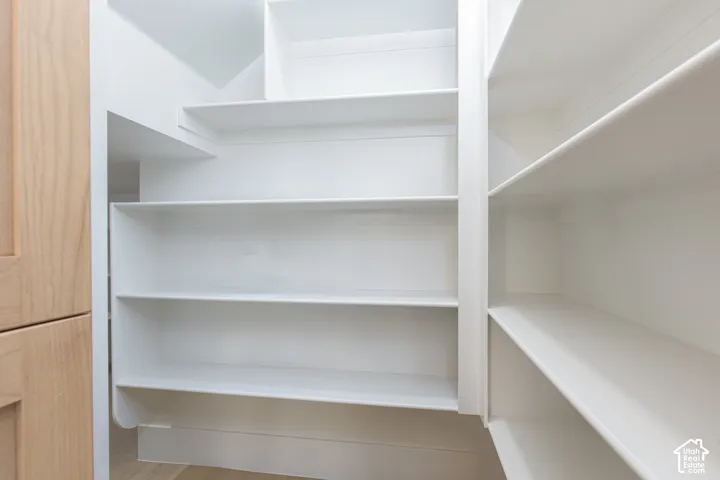 Walk-in storage featuring tiered white shelving and light wood-finish cabinetry