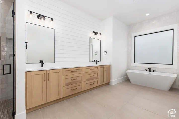 Dual-sink vanity with wood-finish cabinetry, solid-surface countertops, wall-mounted shiplap detailing, freestanding soaking tub, and matte black hardware
