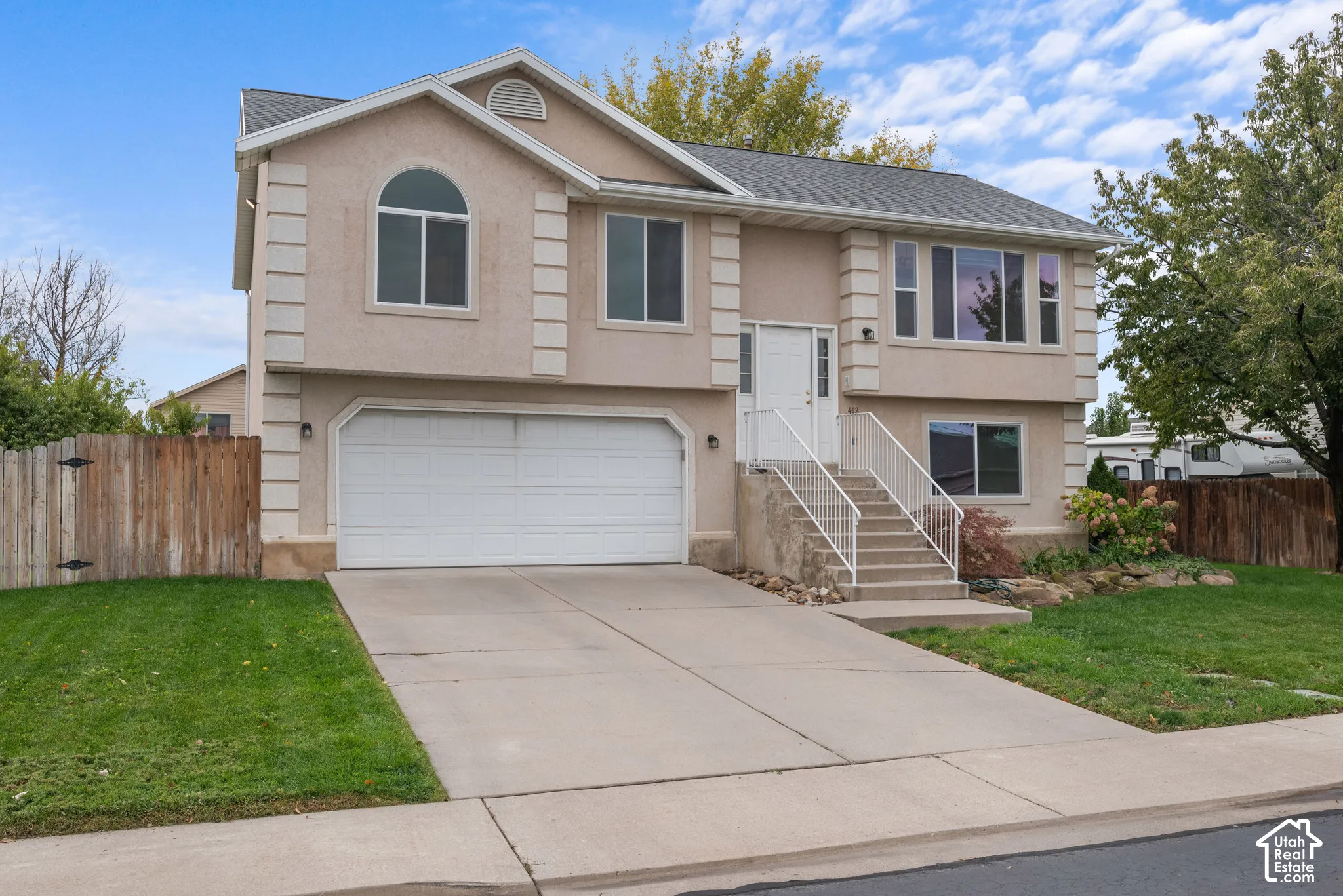 Stucco exterior featuring decorative corner quoins, an attached two-car garage, concrete driveway, and front entryway with metal railings