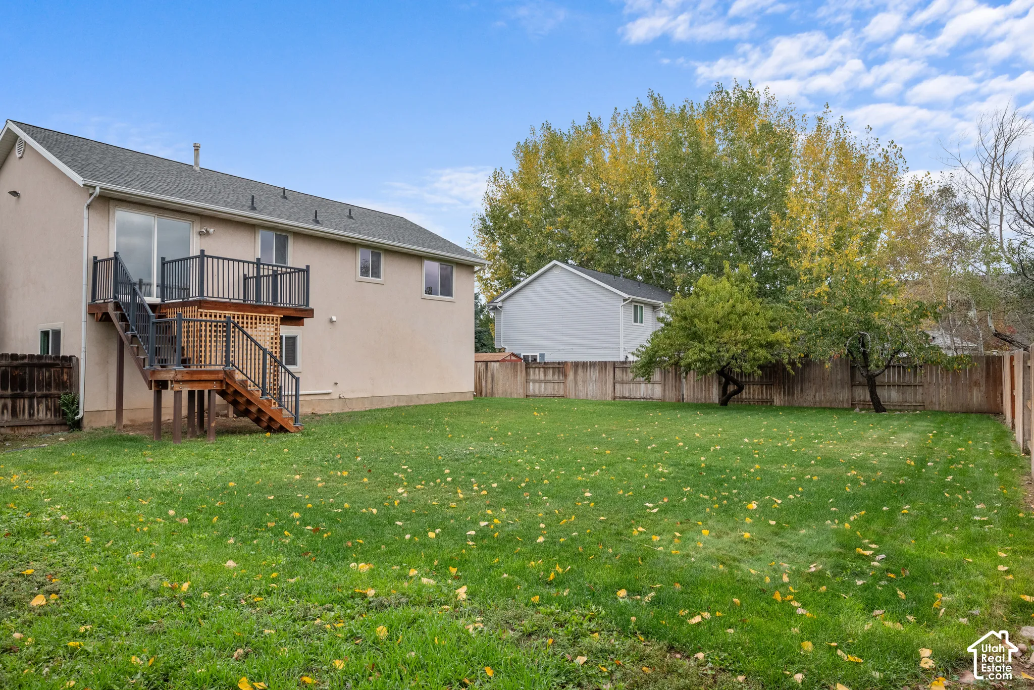 Expansive backyard featuring a large grass lawn, perimeter wood fencing, and elevated rear deck with metal railings