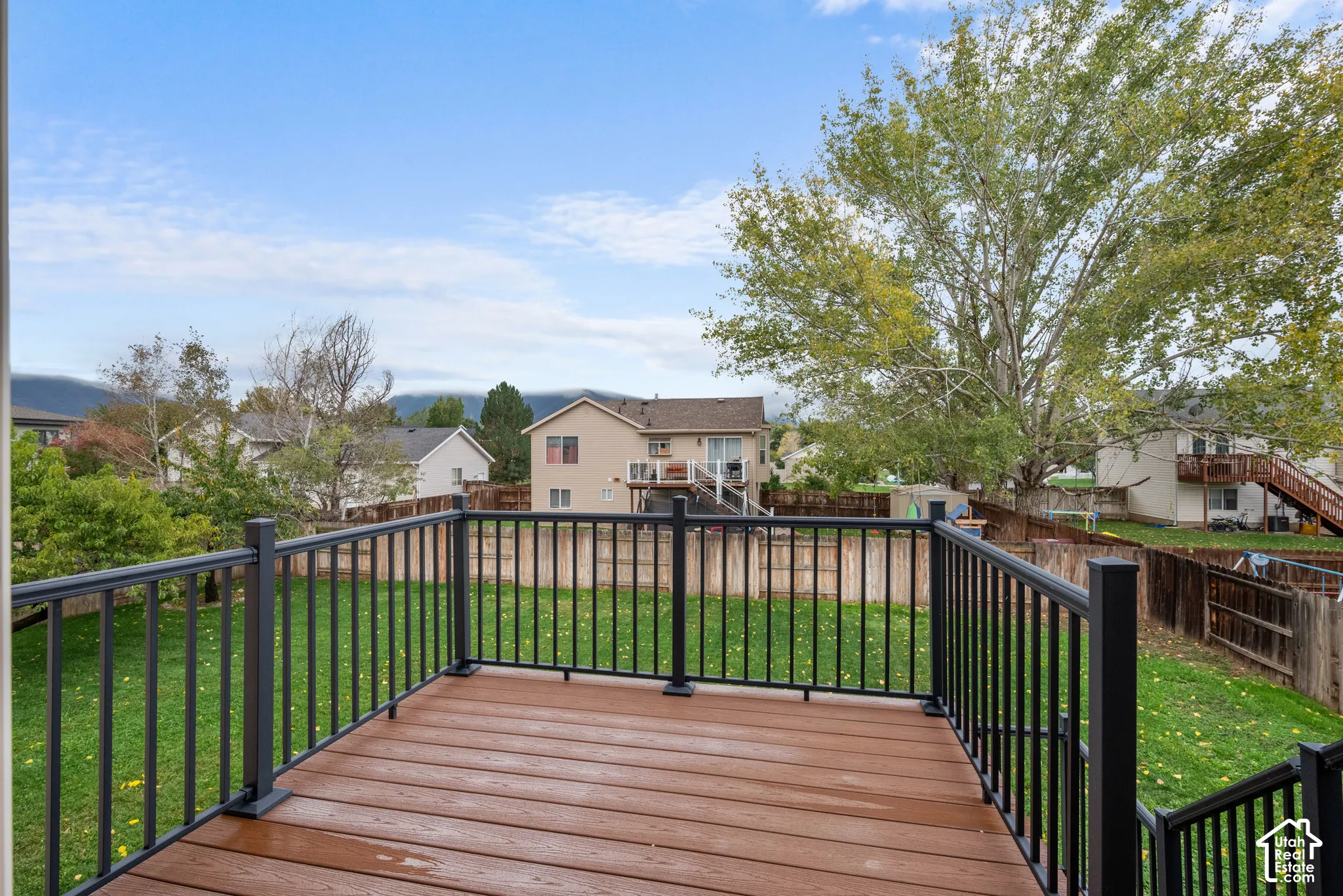 Elevated deck featuring composite decking and a black metal railing, overlooking a fenced backyard with mature trees and a mountain backdrop