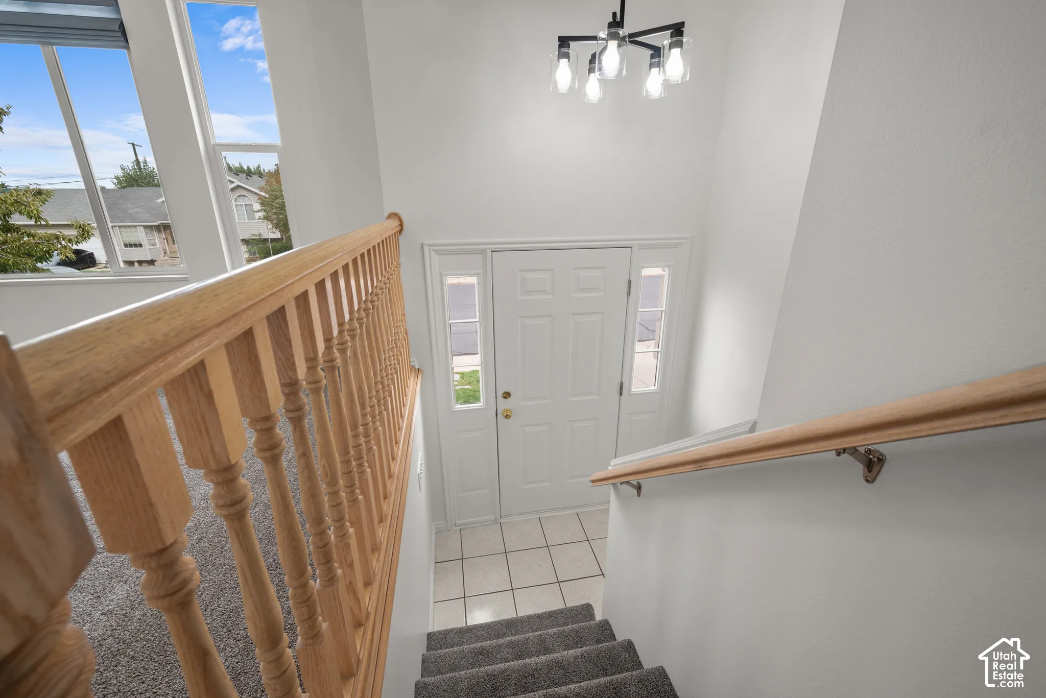 Entryway featuring a solid door with dual sidelights, tile flooring, high ceilings, a multi-light chandelier, and a wood-finish staircase railing