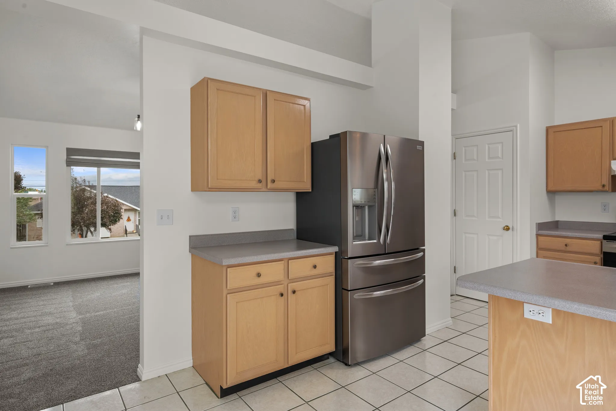 Kitchen featuring light wood-finish cabinetry, solid-surface countertops, stainless steel refrigerator, and tiled flooring