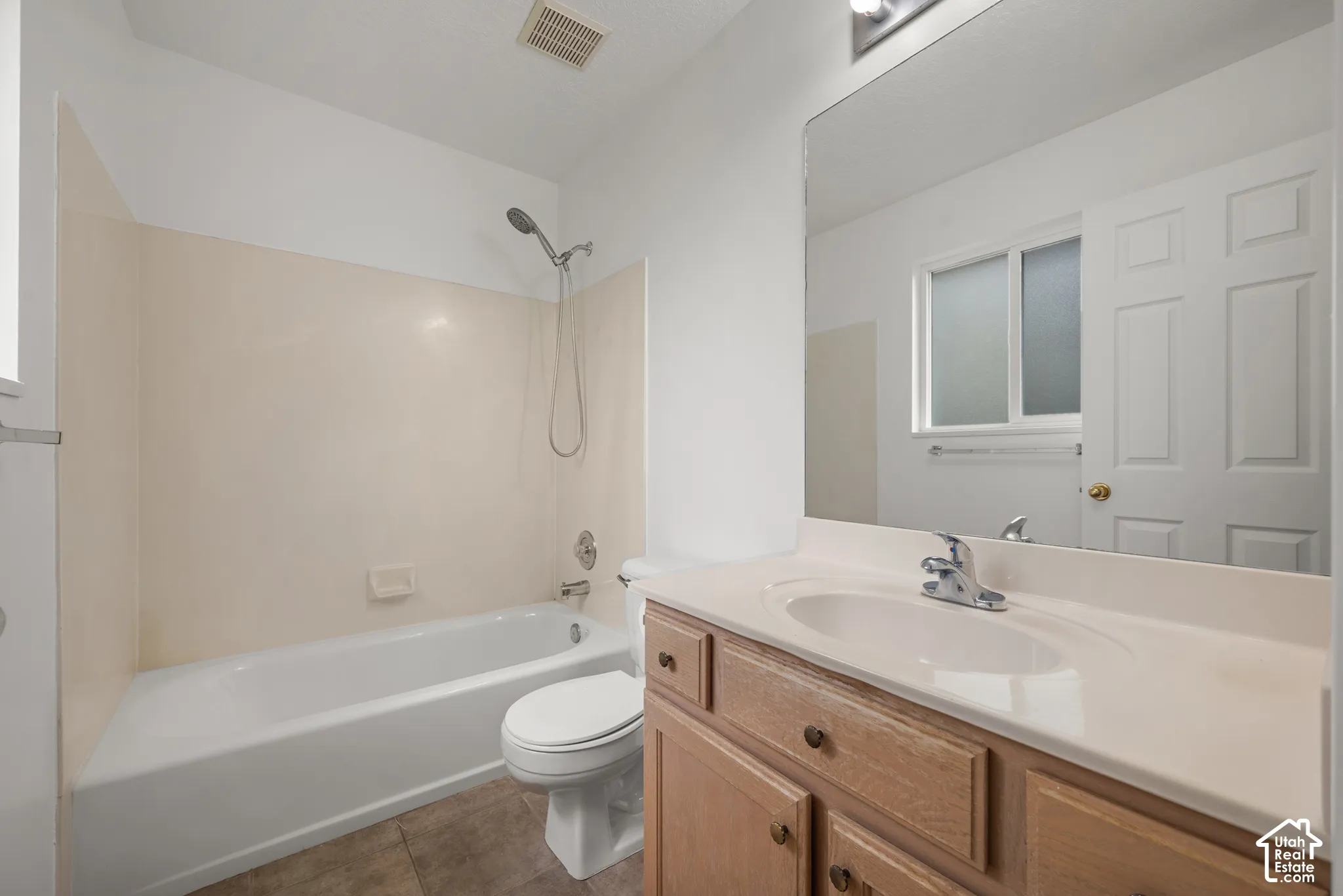Bathroom featuring a wood-finish vanity with a molded countertop, a large wall-mounted mirror, a porcelain bathtub-shower combination with surround panels, and tile flooring