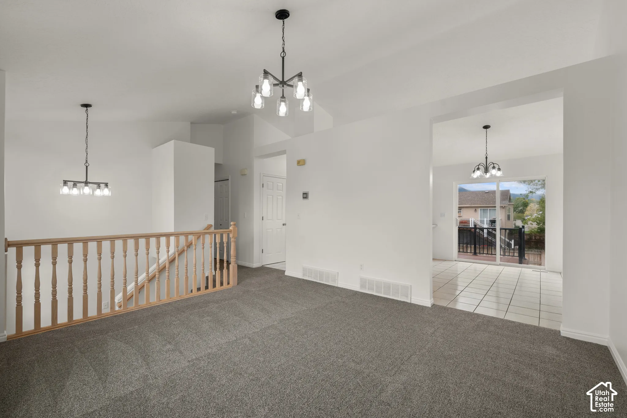 Vaulted ceilings, neutral carpeting, wooden spindle railing, two multi-arm chandeliers, and tile flooring