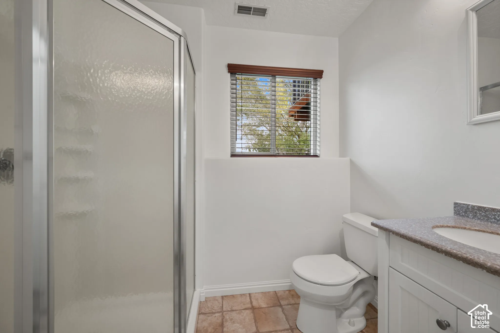 Bathroom featuring a walk-in shower with metal-framed glass doors, a vanity with stone-finish countertop and integrated sink, and ceramic tile flooring