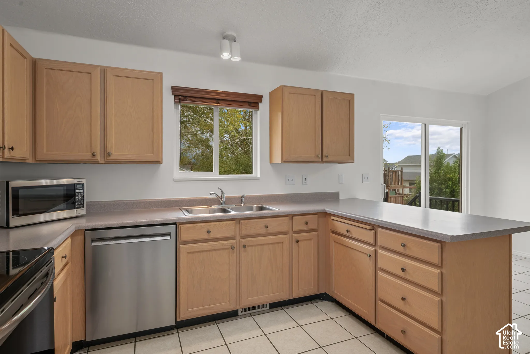Kitchen featuring natural wood cabinetry, solid-surface countertops, stainless steel appliances, ceramic tile flooring, and a sliding glass door