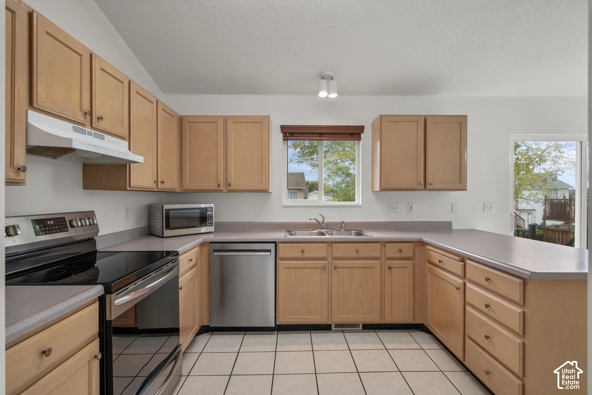 Kitchen featuring wood cabinetry, stainless steel appliances, solid-surface countertops, dual-basin sink, and ceramic tile flooring