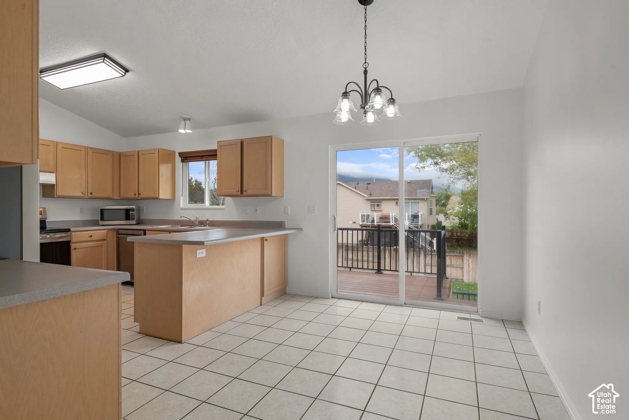 Kitchen featuring wood cabinetry, a peninsula with countertop seating, tiled flooring, a multi-light chandelier, and a sliding glass door