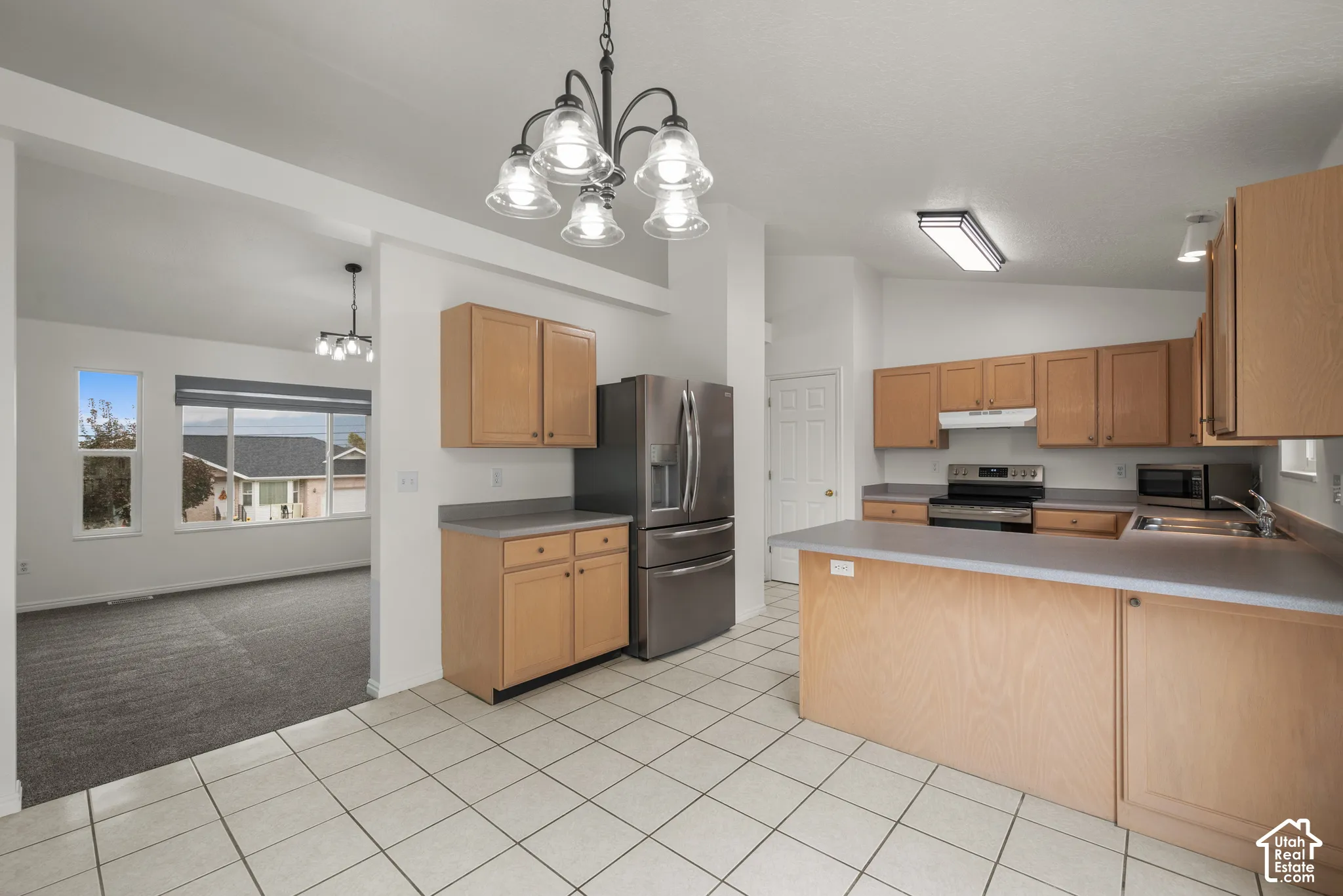 Kitchen featuring light-finish cabinetry, neutral solid-surface countertops, tile flooring, and a stainless steel refrigerator
