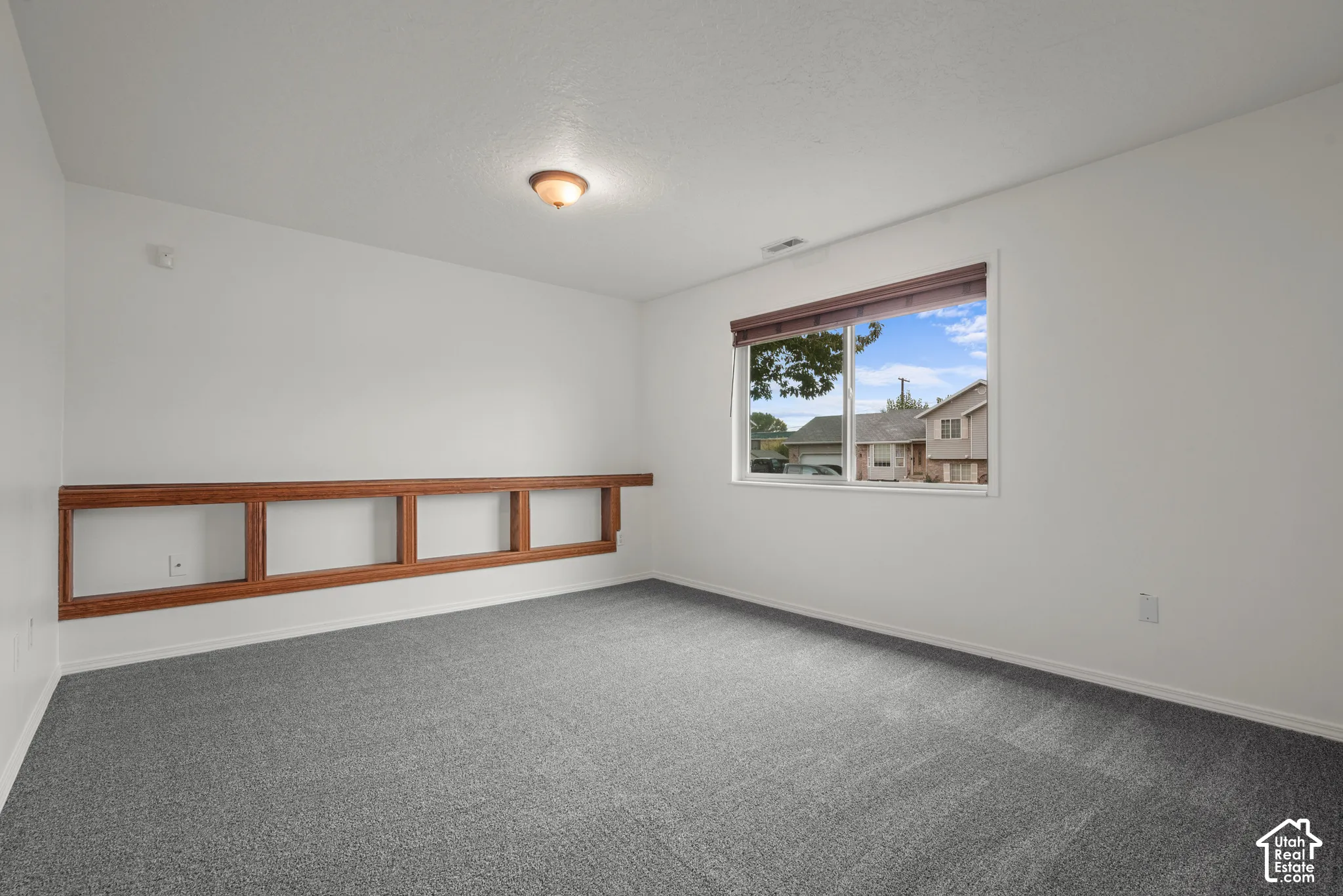 Neutral interior room featuring plush carpeting, a large sliding window with wood-finish blinds, and built-in wood shelving