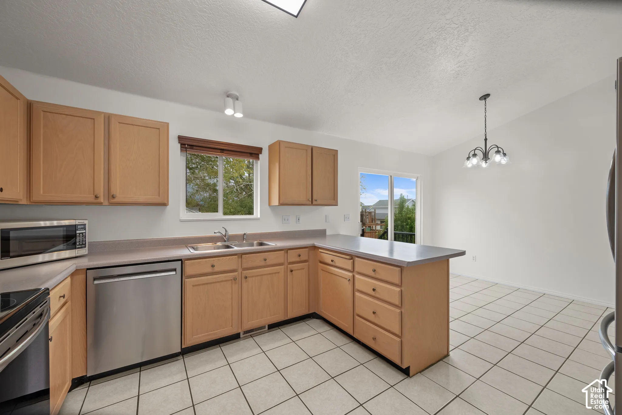 Kitchen featuring light-finish cabinetry, neutral solid-surface countertops, stainless steel dishwasher, ceramic tile flooring, and a multi-light chandelier